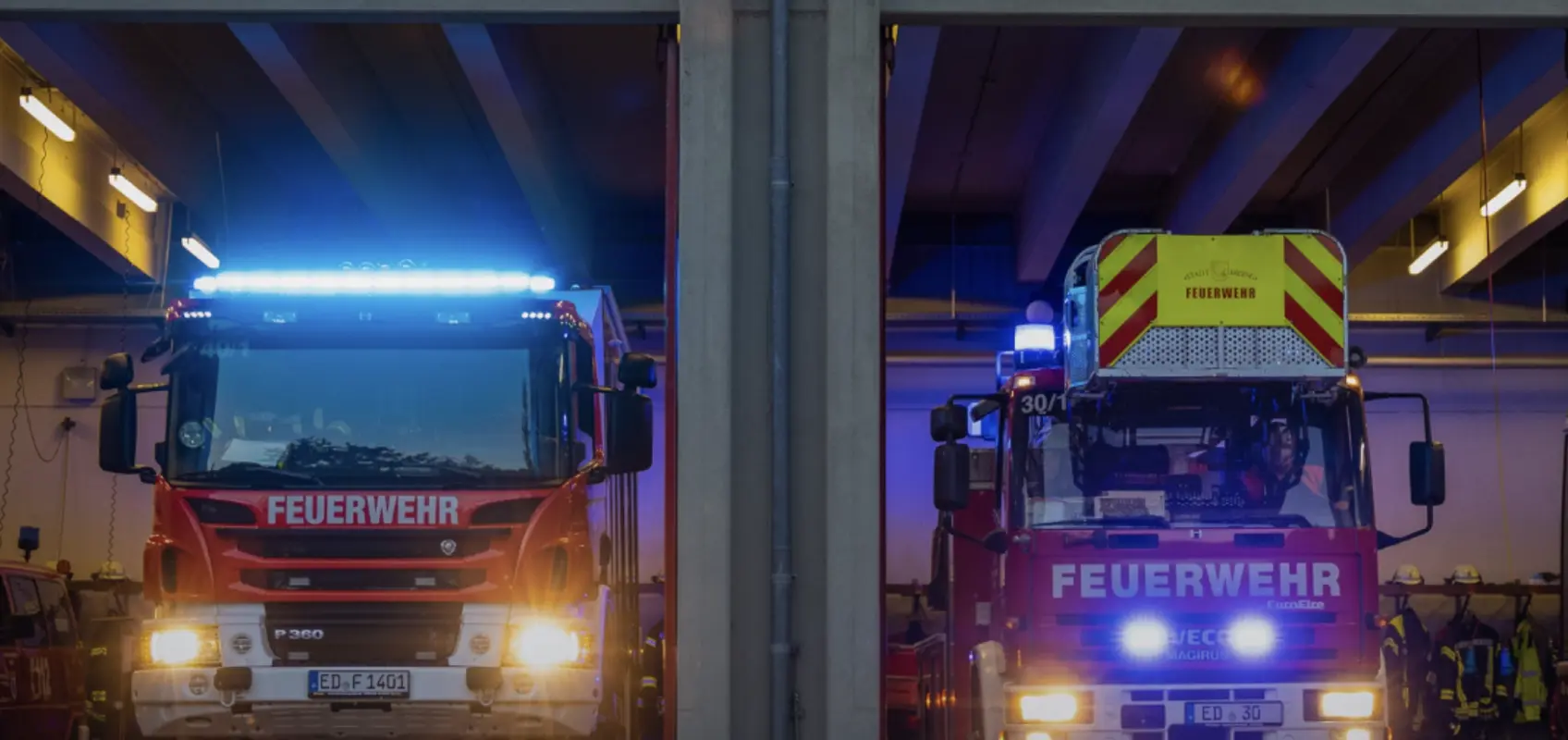 Zwei Feuerwehrfahrzeuge nachts in der beleuchteten Fahrzeughalle der Feuerwehr Erding